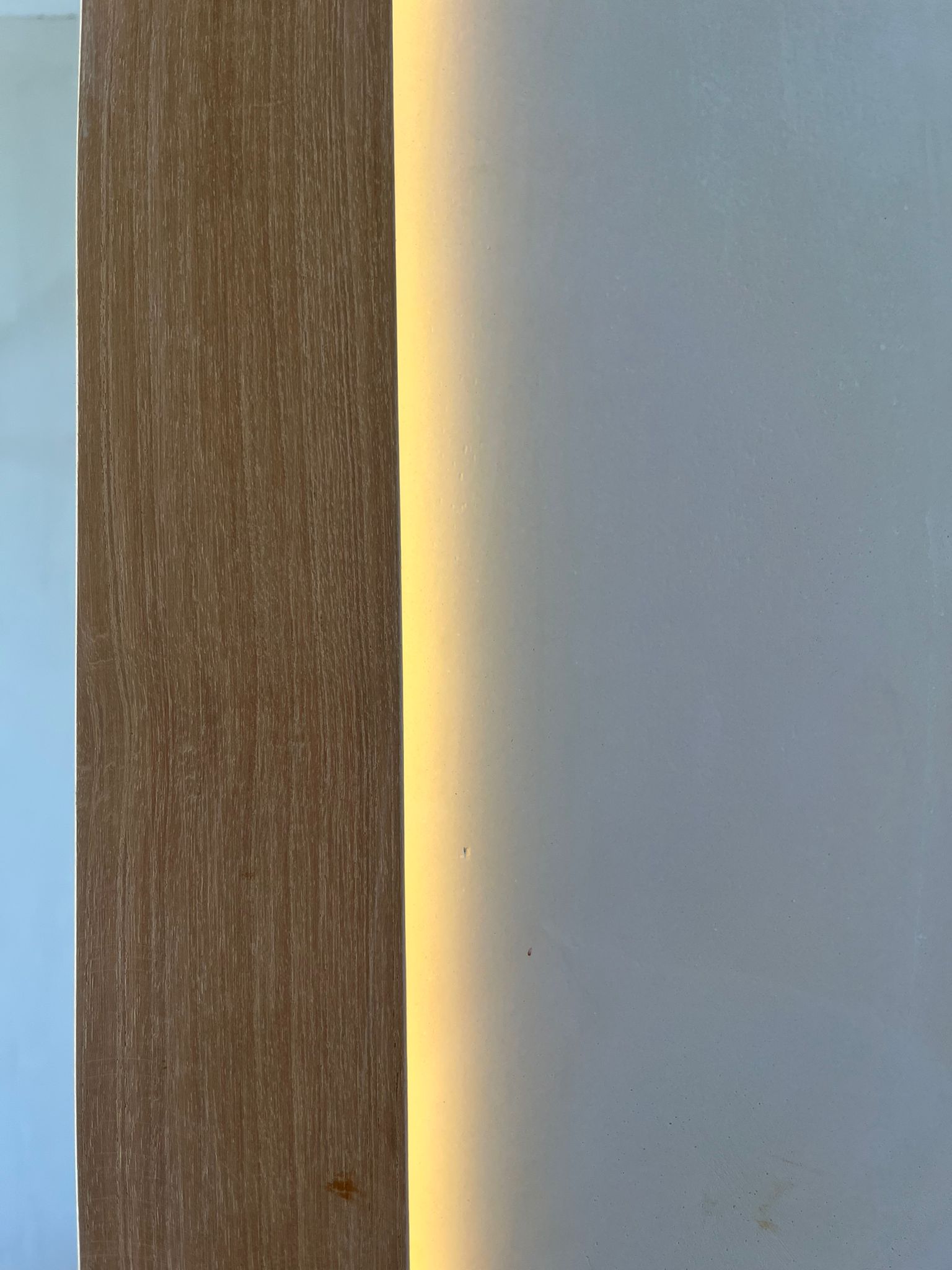 Beige microcement wall beside a wood column with hidden LED grazing light