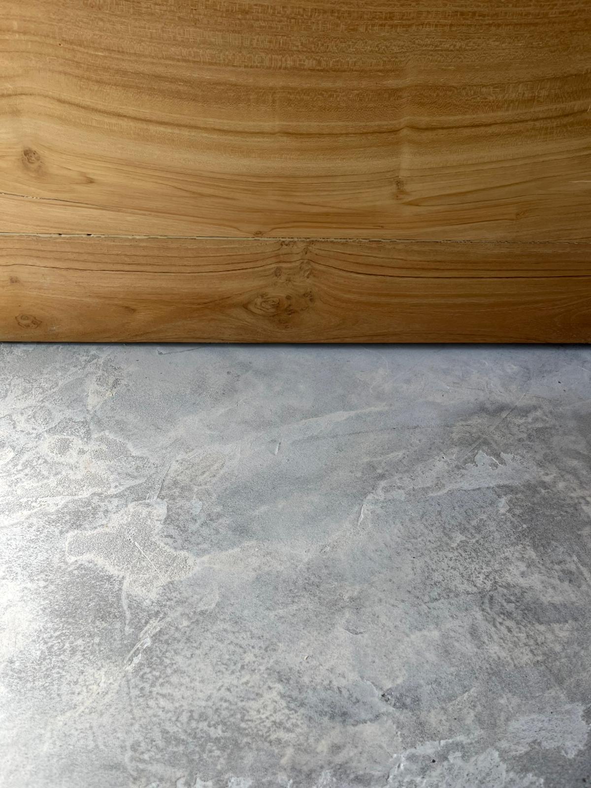 Grey microcement floor meeting a teak-toned wood wall panel