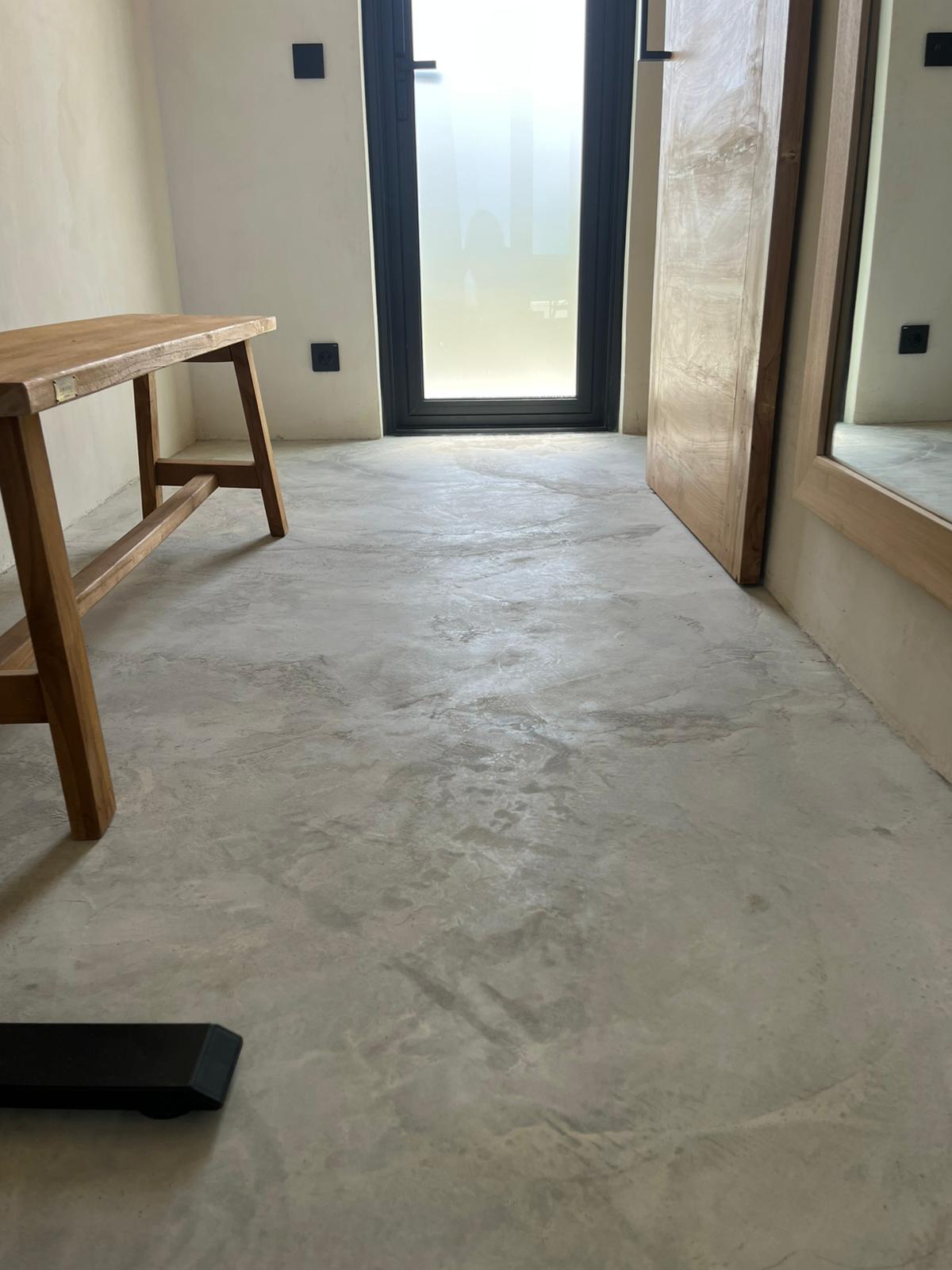 Room interior with seamless light-grey microcement floor, wooden bench and mirror