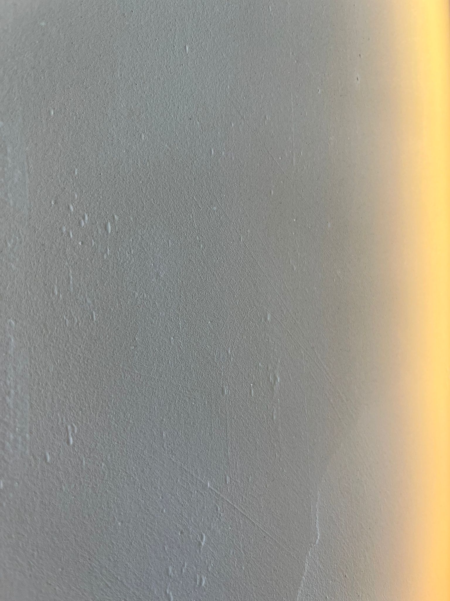 Mid-grey microcement wall with warm light spill on the right edge