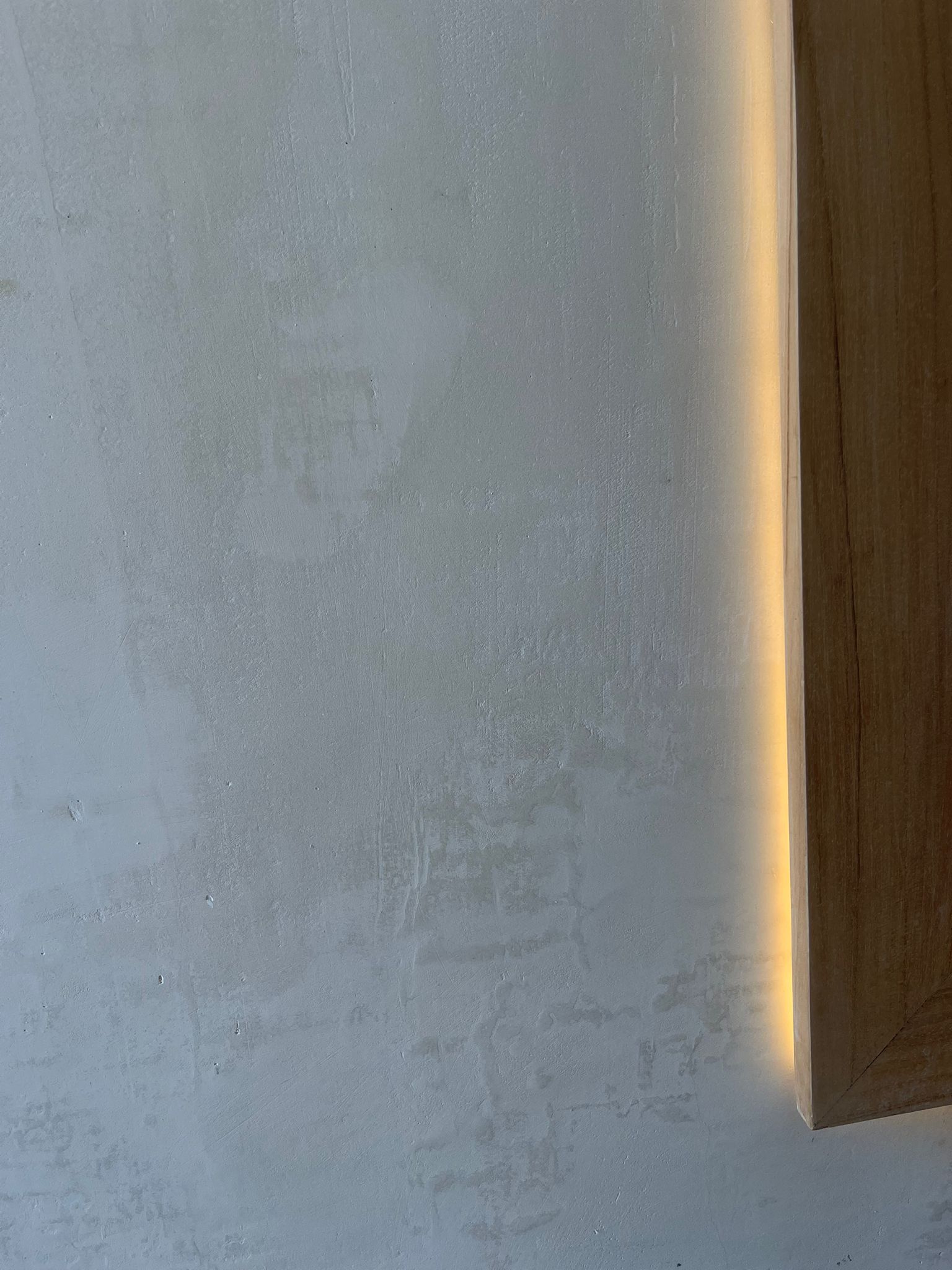 Off-white microcement wall next to wooden frame with warm LED strip